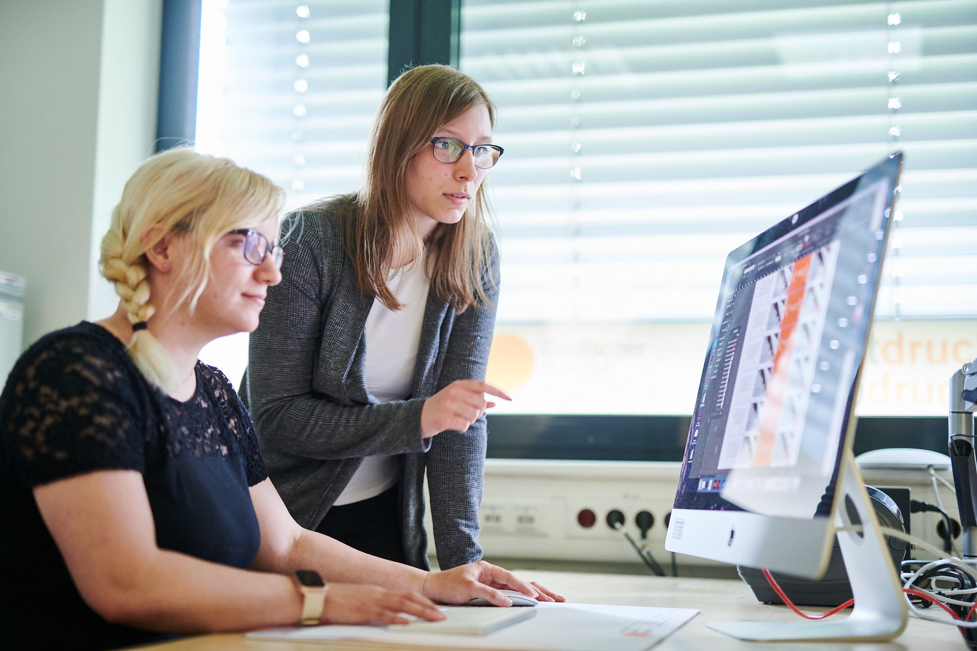 Zwei Mitarbeiter schauen sich am Computer einen Druckbogen an.